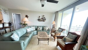A living room with a sectional sofa, a coffee table, and two wicker chairs. There is a ceiling fan, a window with a view, and a door leading to another room. - 3/2 condo Futura Yacht Club Pool, Dockage, Wifi, dockage, beach (Islamorada)