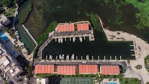 An aerial view of a marina with boats docked, a tennis court, and a building with a red roof.