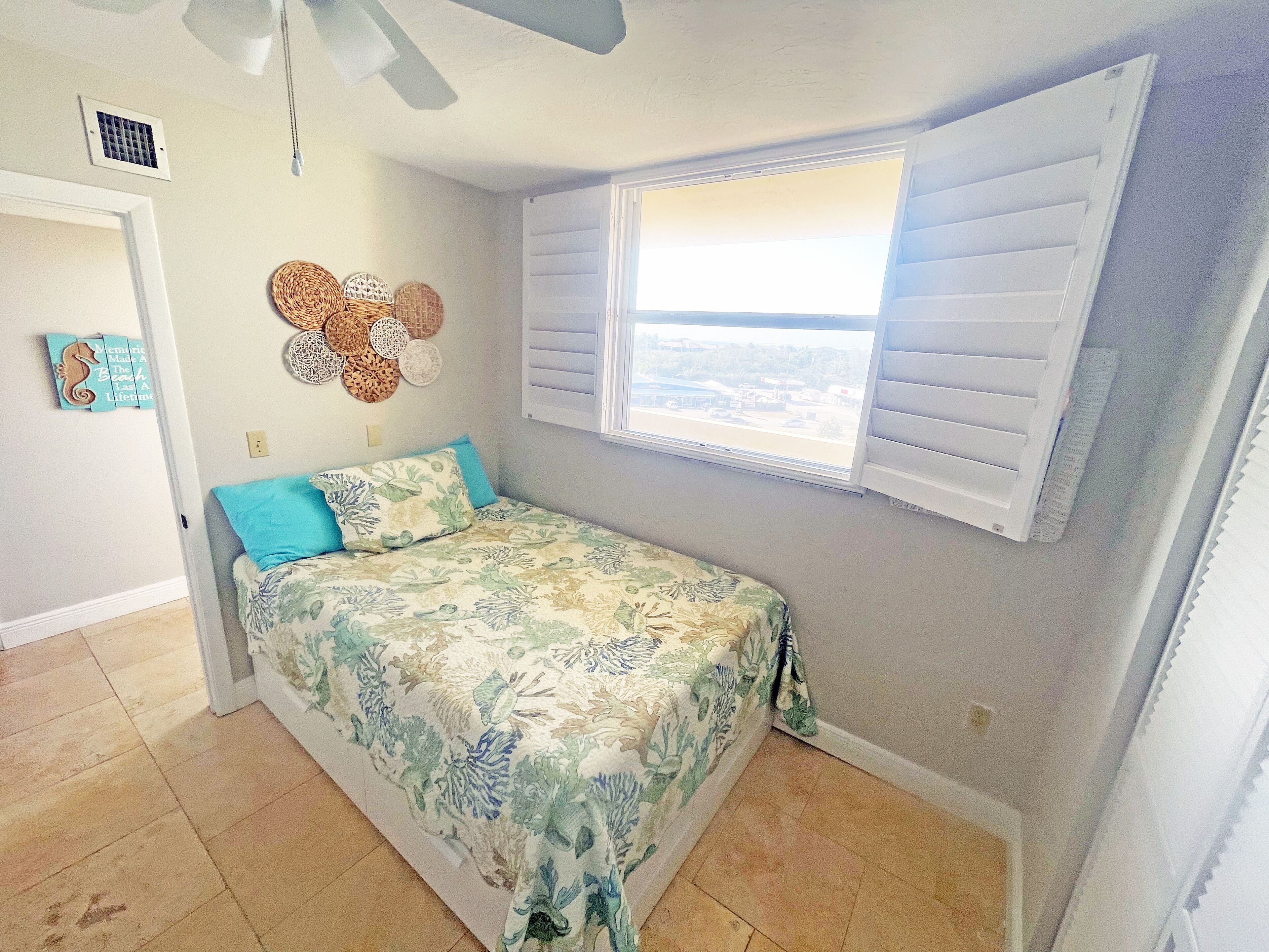 A bedroom with a bed, a window with blinds, a ceiling fan, and a wall decoration.