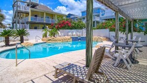 A pool area with a clear blue pool, lounge chairs, and a covered seating area.