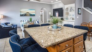A spacious kitchen with a granite island, blue upholstered chairs, and a ceiling fan.