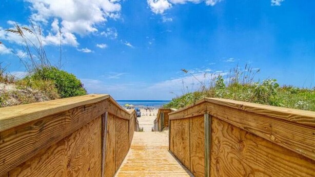 A wooden boardwalk leading to a beach with a clear sky.