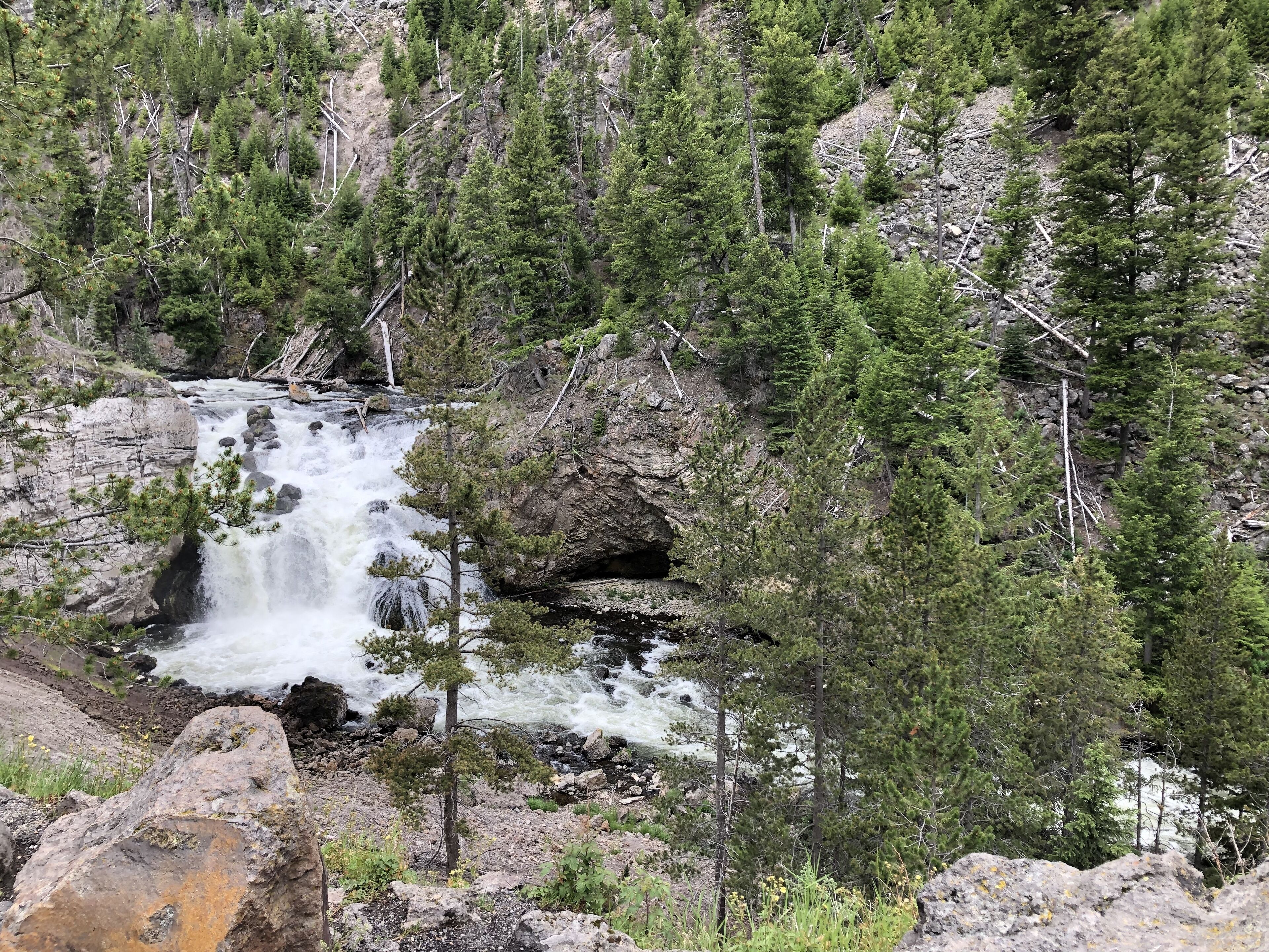A natural landscape with a waterfall, rocky terrain, and dense forest.