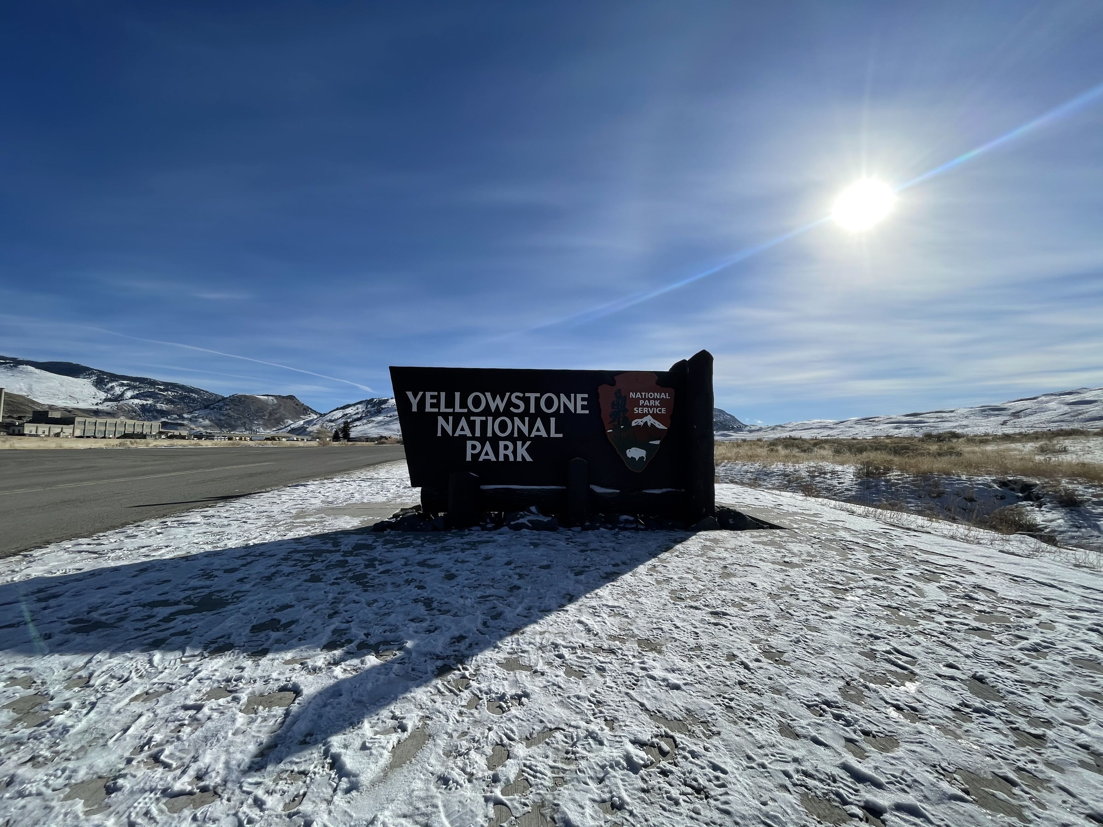 A sign for Yellowstone National Park with a clear sky and mountains in the background.