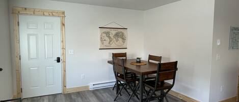A dining area with a wooden table and chairs, a world map on the wall, and a white door.