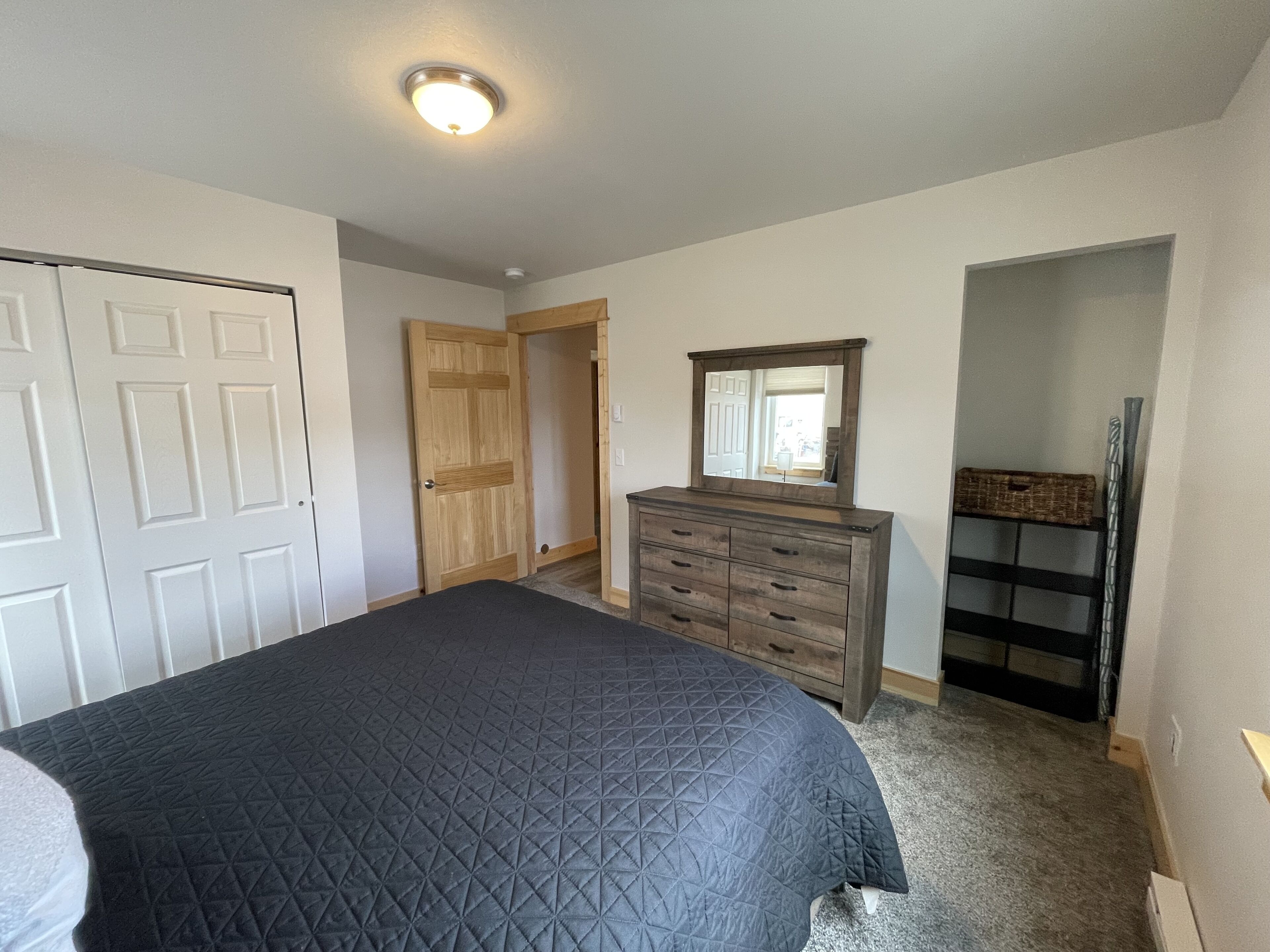 A bedroom with a bed, dresser, mirror, and a door leading to another room.