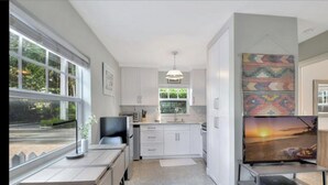 A modern kitchen with white cabinets, a dining area with a table and chairs, and a large window providing a view of greenery outside.