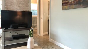 A living room with a flat-screen TV on a stand, a white vase with a plant, and a painting on the wall.