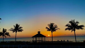A beach scene with a gazebo, palm trees, and the ocean at sunset.