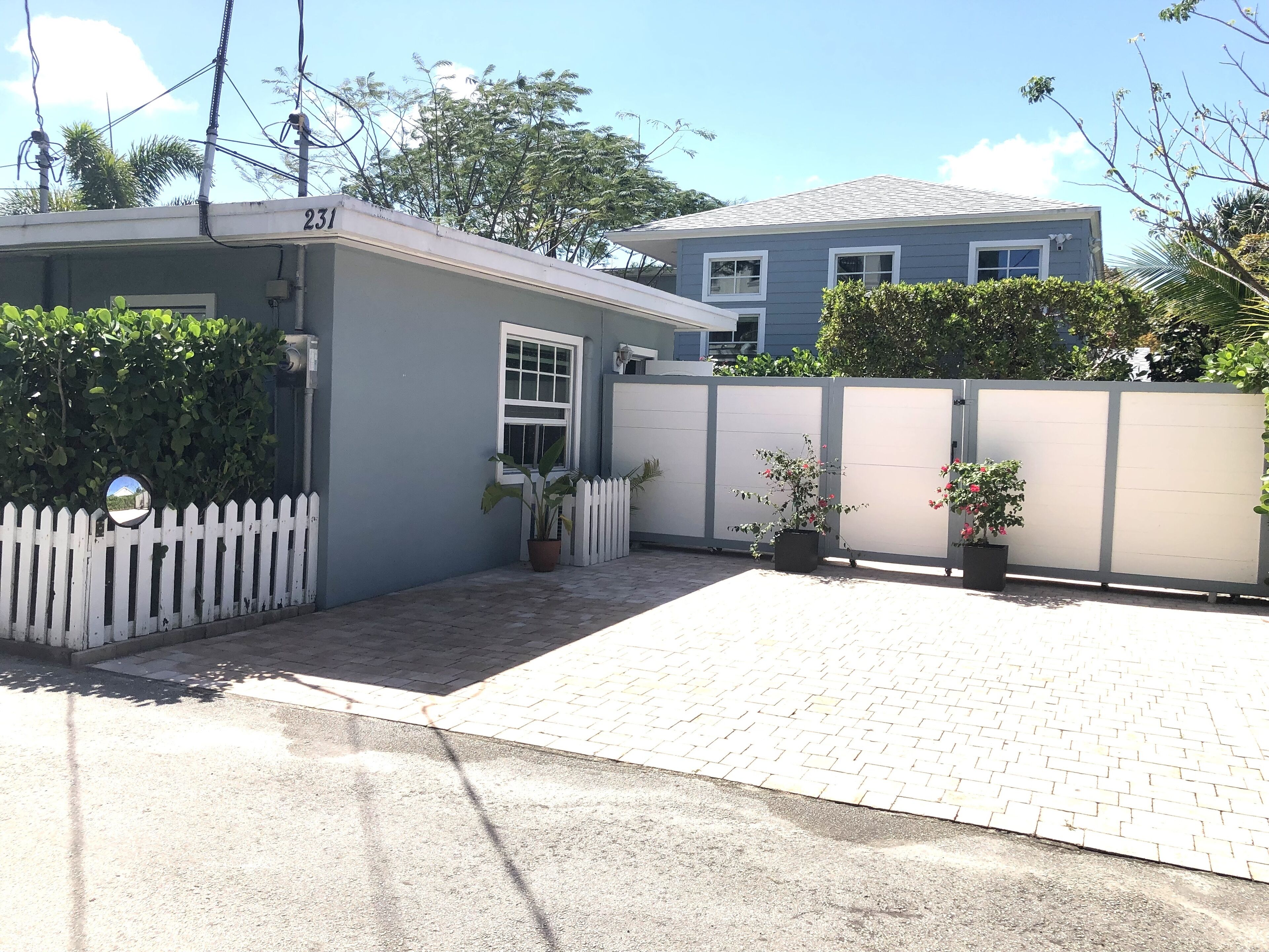 A residential area with a house number 231, a white picket fence, and potted plants.