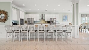 A spacious kitchen with white cabinetry, a central island with bar stools, and modern appliances. - Pineapple Palace, Luxury Oceanfront Beach House with Pool and Hot Tub (North Myrtle Beach)