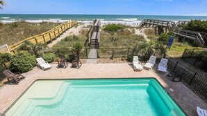 A pool area with a view of the ocean, surrounded by a wooden deck and lounge chairs. - Pineapple Palace, Luxury Oceanfront Beach House with Pool and Hot Tub (North Myrtle Beach)