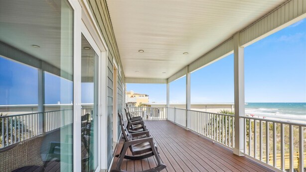 A covered balcony with wooden flooring, glass railings, and a view of the beach. - Pineapple Palace, Luxury Oceanfront Beach House with Pool and Hot Tub (North Myrtle Beach)