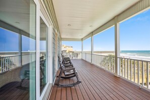 Un balcón cubierto con suelo de madera, barandillas de cristal y vistas a la playa.