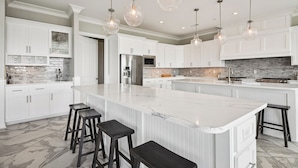 Una cocina moderna con armarios blancos, una isla grande con taburetes de bar e iluminación colgante.
