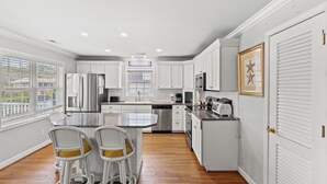 A modern kitchen with white cabinetry, stainless steel appliances, and a central island with bar stools.