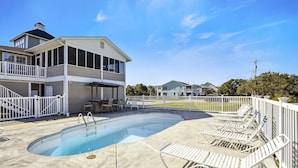 A two-story building with a swimming pool, outdoor seating, and a fenced patio area.