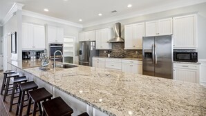 Une cuisine moderne avec des meubles blancs, des appareils en acier inoxydable et un îlot en granit doté de tabourets de bar.