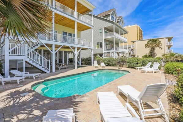 A pool area with a two-story building, outdoor seating, and a staircase.