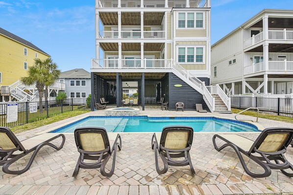 A pool area with lounge chairs, a small pool, and a multi-story building with balconies.