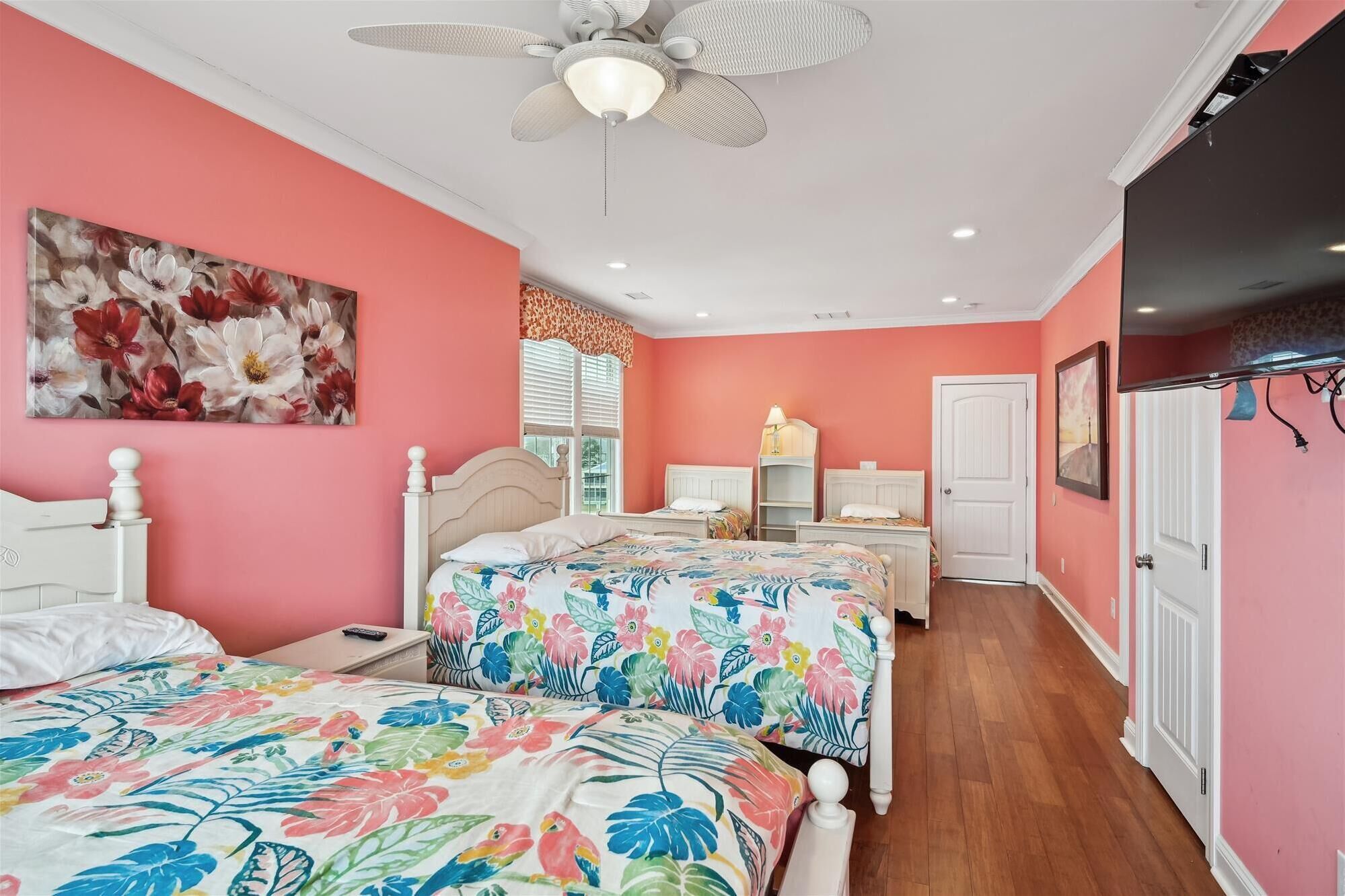 A bedroom with two beds, a ceiling fan, and a large floral painting on the wall.