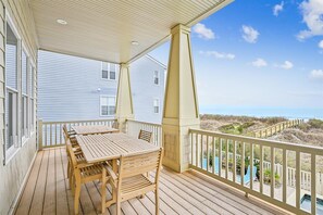 A wooden deck with a table and chairs, overlooking a beach with a wooden fence and a clear sky. - Sun Sand & Sea, an Oceanfront 9BR House with Private Pool. (North Myrtle Beach)