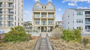A multi-story building with a central porch, a staircase leading to the entrance, and a wooden boardwalk in front. - Sun Sand & Sea, an Oceanfront 9BR House with Private Pool. (North Myrtle Beach)