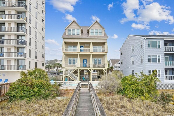 A multi-story building with a central porch, a staircase leading to the entrance, and a wooden boardwalk in front. - Sun Sand & Sea, an Oceanfront 9BR House with Private Pool. (North Myrtle Beach)