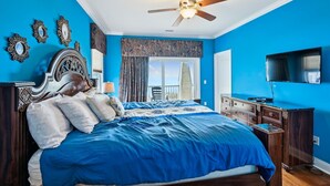 A bedroom with a large bed, a ceiling fan, a TV, and a view of the outdoors. - Sun Sand & Sea, an Oceanfront 9BR House with Private Pool. (North Myrtle Beach)