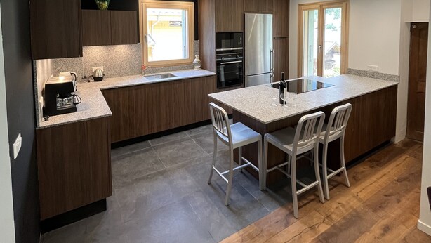 Una cocina moderna con armarios de madera oscura, encimera de granito y una isla central con taburetes de bar.