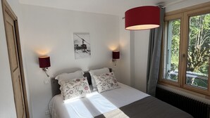 Un dormitorio con una cama, dos lámparas de pared, una ventana con vista a follaje e iluminación en el techo.