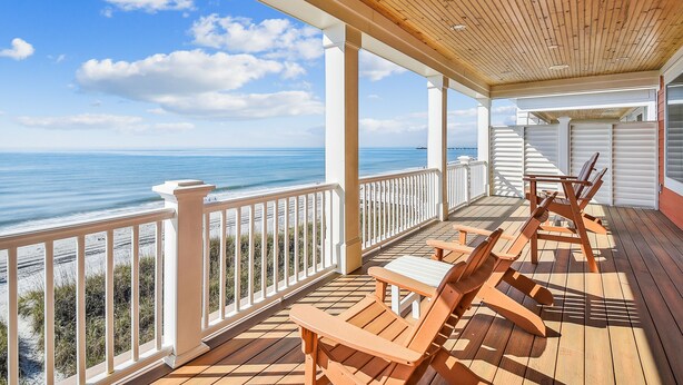 A covered outdoor deck with wooden furniture and a view of the ocean. - Living Beach 2, Luxury Oceanfront Home in Cherry Grove with Game Room and Pool (North Myrtle Beach)