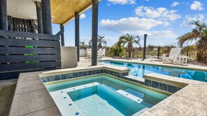 A pool area with a hot tub, lounge chairs, and palm trees. - Living Beach 2, Luxury Oceanfront Home in Cherry Grove with Game Room and Pool (North Myrtle Beach)