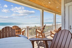 Une terrasse en bois, agrémentée de chaises et de tables, qui offre une vue sur la plage.