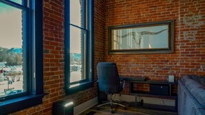 Ein Zimmer mit Backsteinwand, großem Fenster, Schreibtisch und Stuhl.