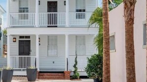 Un bâtiment blanc à deux étages, doté d’un balcon au deuxième étage, entouré de palmiers et de plantes en pot.