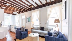 Un salon moderne avec un canapé, des fauteuils, une table basse et une cuisine en arrière-plan.