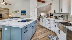 Een ruime keuken met witte kastjes, een marmeren eiland en een houten plafond.
