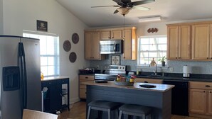 A modern kitchen with wooden cabinets, a stainless steel refrigerator, a microwave, and a ceiling fan. - Paradise on the Bayou at the Bat Cave! (Slidell)