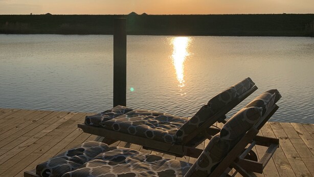 A wooden deck with two lounge chairs facing a calm body of water at sunset. - Paradise on the Bayou at the Bat Cave! (Slidell)