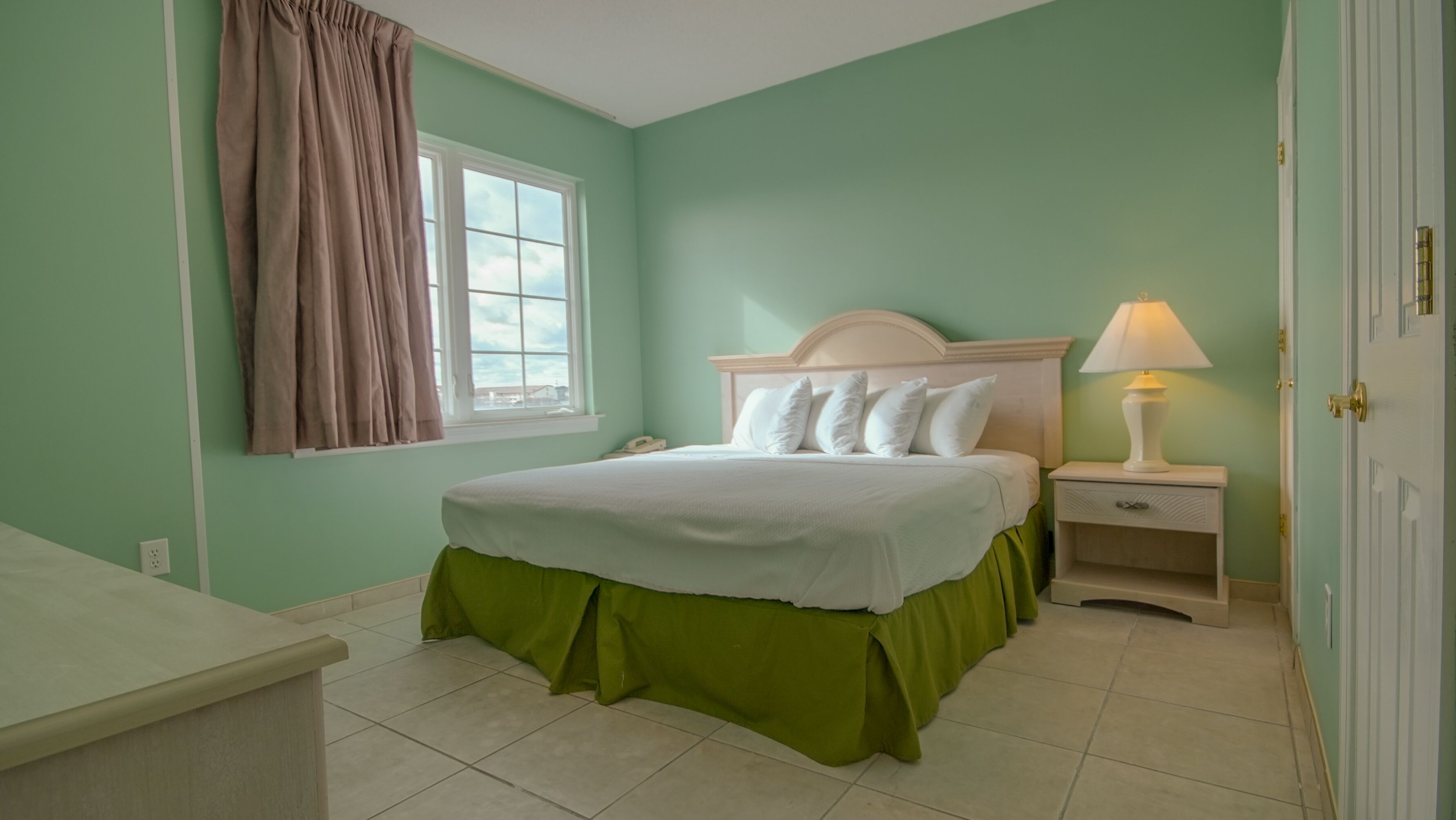 Une chambre à coucher avec un lit, une table de chevet, une lampe et une fenêtre avec des rideaux.