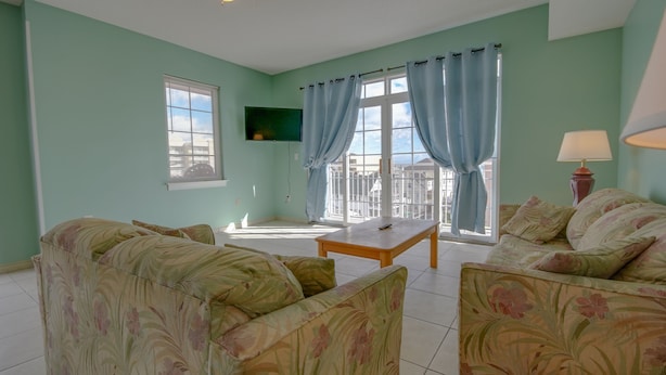 A living room with floral-patterned sofas, a wooden coffee table, and a TV mounted on the wall. - Americana Princess Suites and Condos (Ocean City)