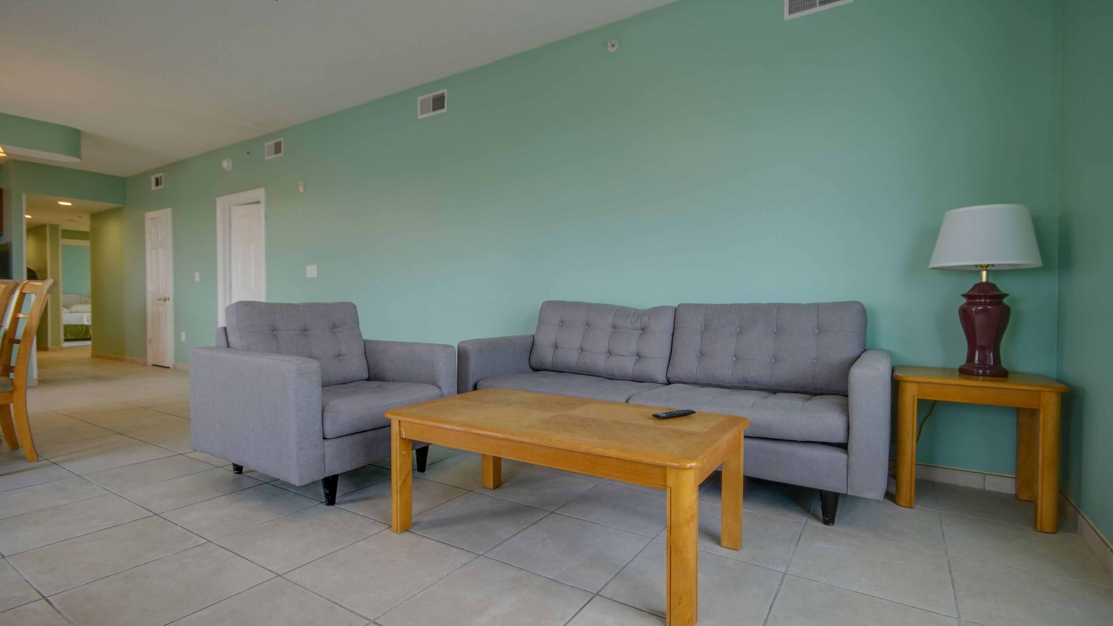 A living room with two grey sofas, a wooden coffee table, and a lamp on a wooden side table.