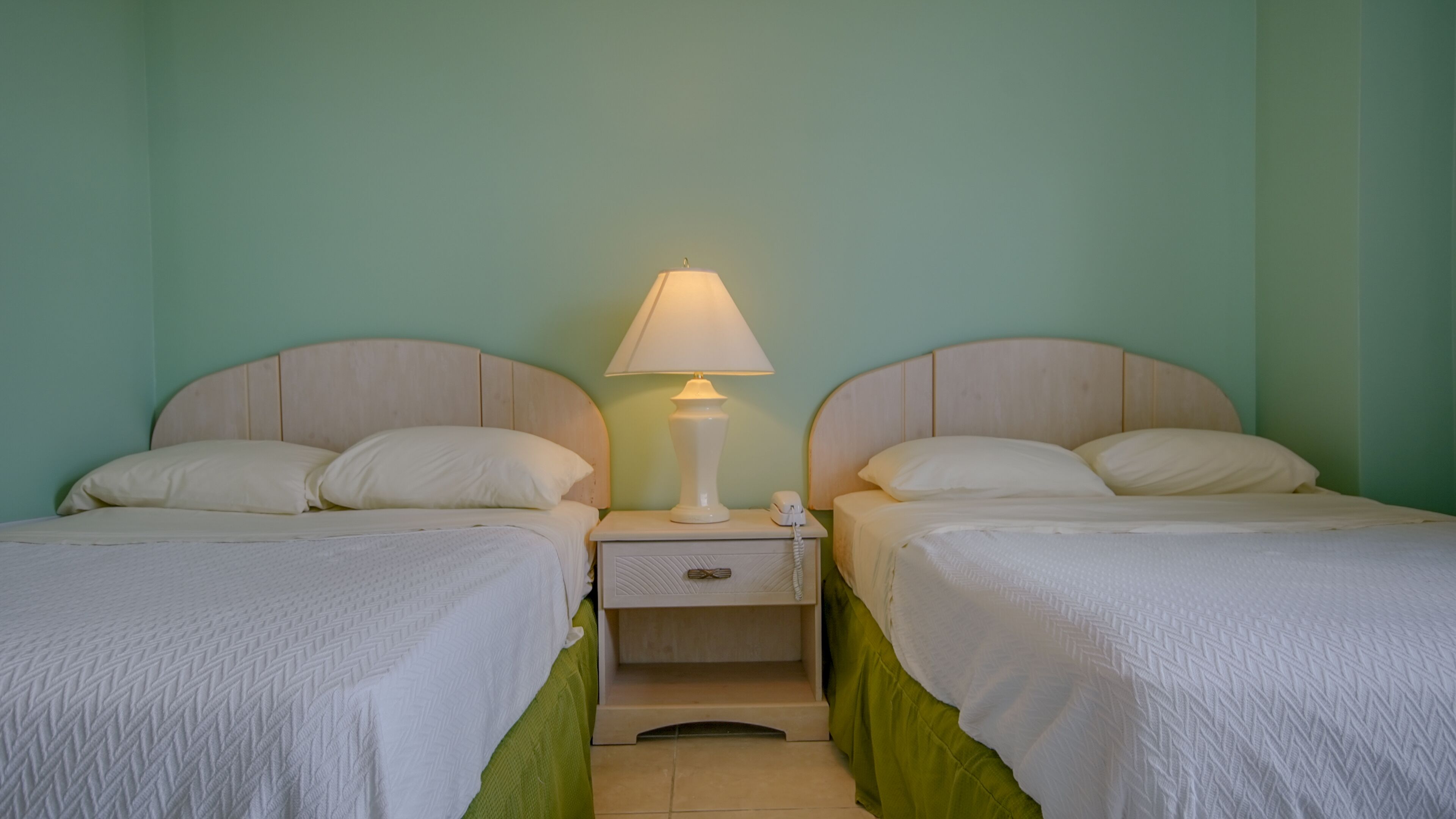 Ein Doppelzimmer mit zwei Betten, einem Nachttisch mit Lampe und einer kleinen Schublade.