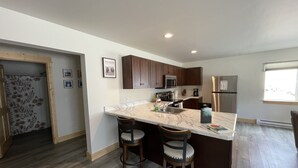 A modern kitchen with a marble countertop, wooden cabinets, stainless steel appliances, and a built-in island with bar stools.