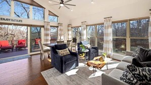A spacious living room with a large window, a ceiling fan, and a fireplace. - The Lakeview Retreat - Lake Access (Eureka Springs)