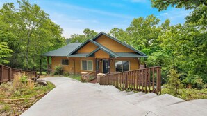 A two-story house with a wooden deck, a stone pathway leading to the front door, and a surrounding wooded area. - The Lakeview Retreat - Lake Access (Eureka Springs)