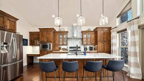A kitchen with wooden cabinets, a stainless steel refrigerator, a marble island with bar stools, and pendant lighting. - The Lakeview Retreat - Lake Access (Eureka Springs)