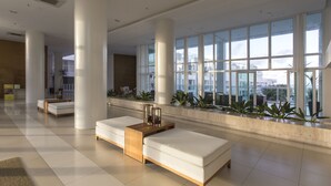 A spacious lobby with large windows, white columns, and a seating area with a wooden side table. - Apartamento Novo e Decorado In Mare Bali (Parnamirim)