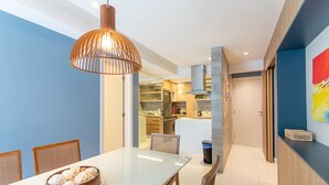 A modern dining area with a glass table, wooden chairs, and a decorative cake centerpiece. - Apartamento Novo e Decorado In Mare Bali (Parnamirim)